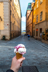 Cropped hand holding ice cream against buildings