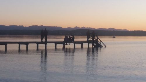 Silhouette people on sea against clear sky during sunset