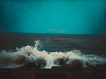 Sea waves splashing on shore against sky