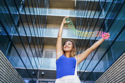 Low angle view of young woman exercising with coiled spring against building