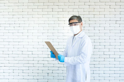 Man holding umbrella while standing by brick wall