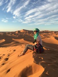 Woman sitting on sand dune in desert against sky