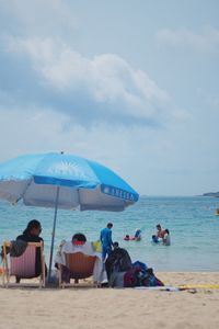 People relaxing on beach against sky