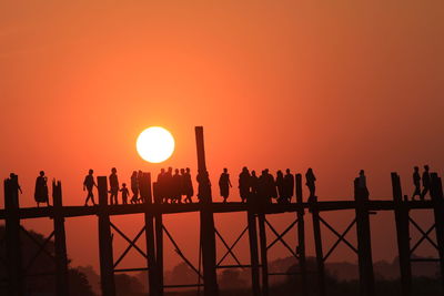 Silhouette monks and people on u bein bridge over river during sunset