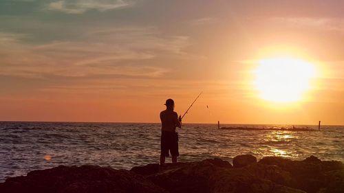 Silhouette man fishing in sea against sunset sky