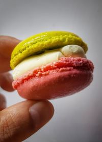 Close-up of hand holding macaroon against white background