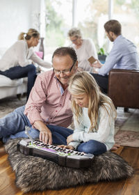 Grandfather and granddaughter playing piano with family in background at home