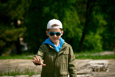 Portrait of boy with sunglasses and cap gesturing while against trees