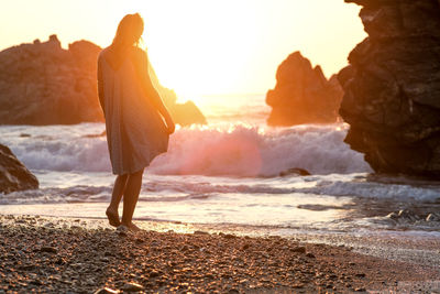 Girl in green dress seen from behind entering a beach at sunset