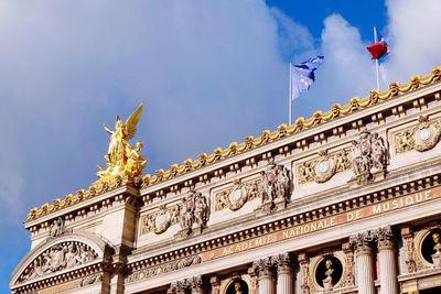 Low angle view of gold statue with flags at palais garnier against sky