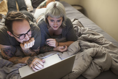 Young couple lying in bed looking at a laptop