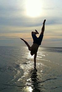 Silhouette of woman jumping on beach at sunset