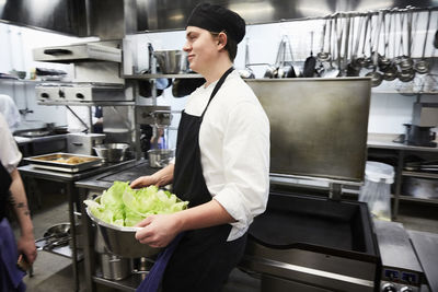 Side view of male chef student holding container of vegetables at commercial kitchen