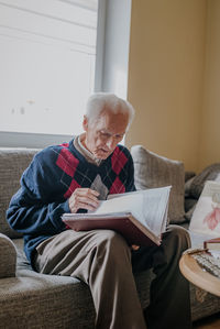 Senior man reading book while sitting on sofa