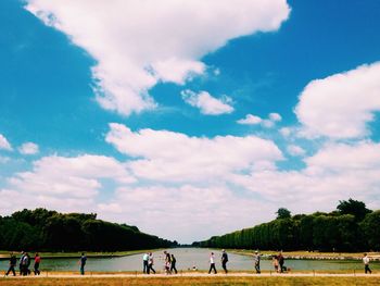 People by lake against cloudy sky