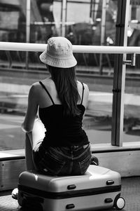 Rear view of teenage girl sitting on suitcase outdoors