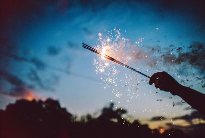 Close-up of silhouette hand holding sparklers against sky at night