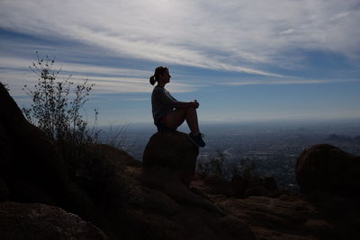 Woman sitting on rock against sky