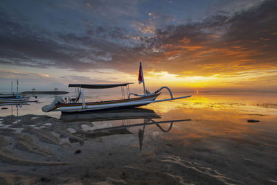 Boat moored on shore against sky during sunset