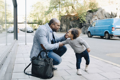 Cheerful father talking to daughter on sidewalk at city