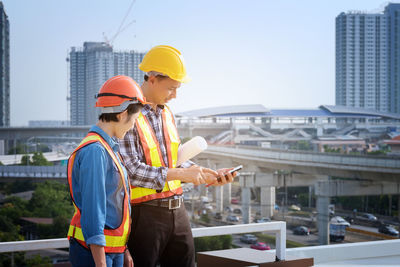 Engineers using mobile phone while standing against buildings in city