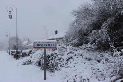 Road sign on snow covered field against sky