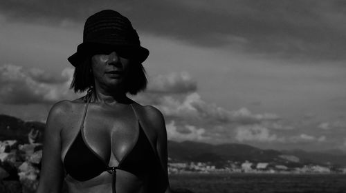 Portrait of woman in bikini standing at beach against sky