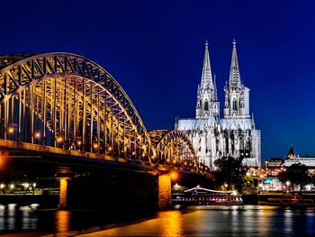Illuminated bridge and buildings at night in cologne with cathedral and blue night sky 