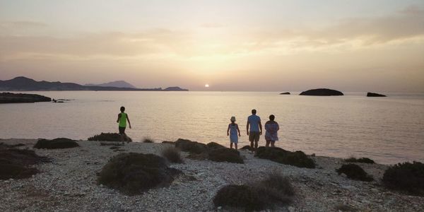 People at beach against sky during sunset