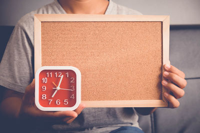 Midsection of woman holding alarm clock and picture frame