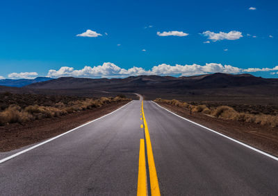 Road leading towards mountain range against blue sky