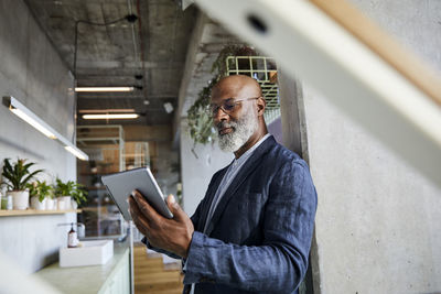 Mature man using digital tablet while standing at home