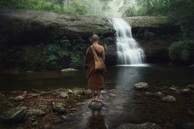 Rear view of woman standing against waterfall