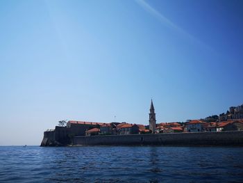 Buildings by sea against clear blue sky