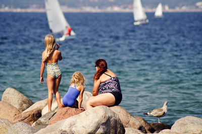 Rear view of friends sitting on rock at beach