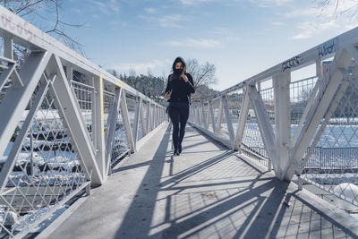 Full length portrait of young woman standing on footbridge