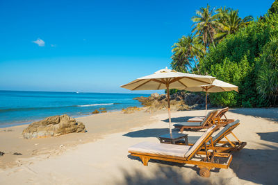 Pair of deck chairs with sun umbrellas at tropical beach with palm trees at sunny day