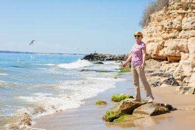 Senior woman in sunglasses stands on the beach and looks at the sea