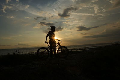 Silhouette man riding bicycle on beach against sky during sunset