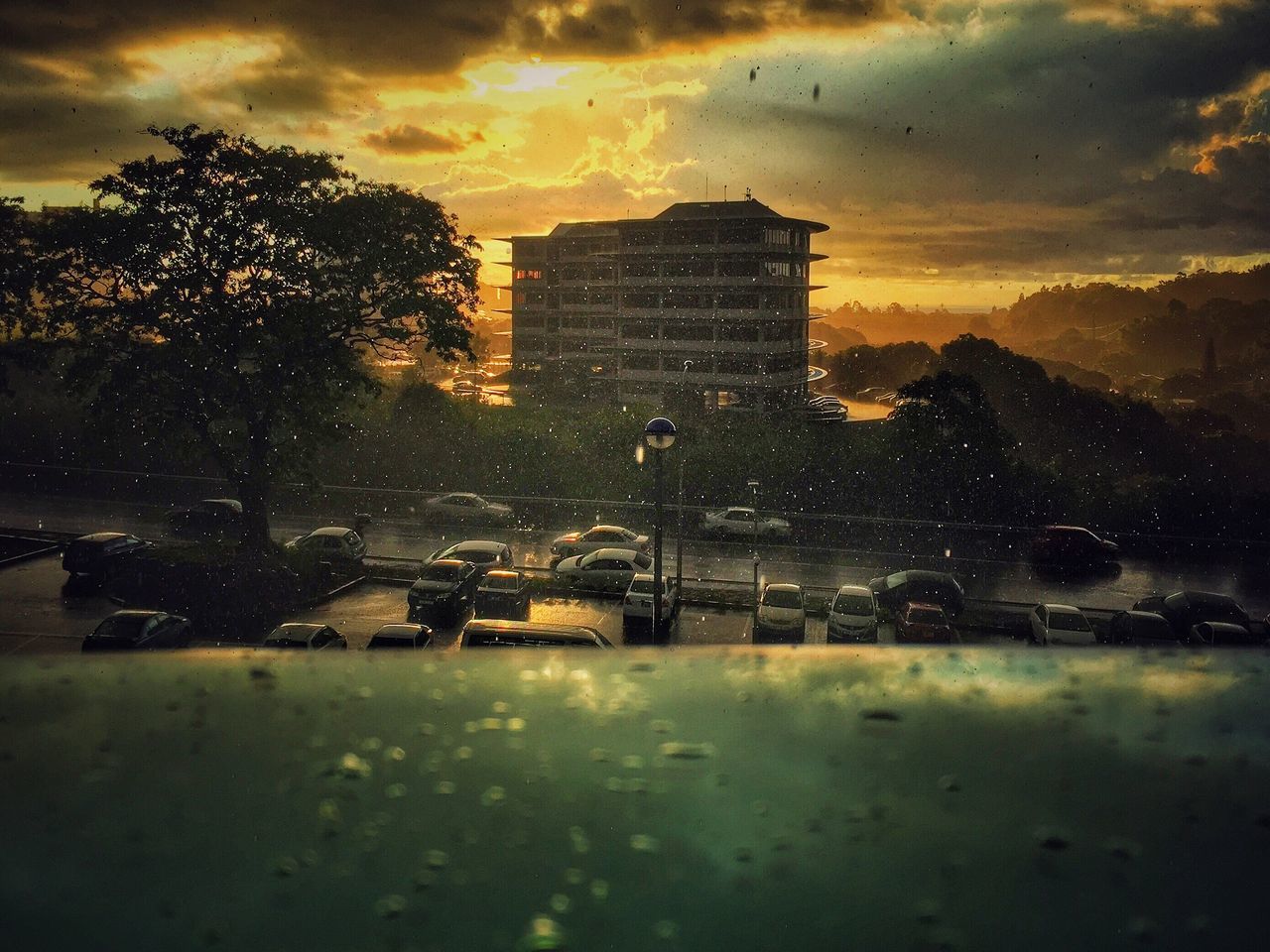 Rain in city against sky during sunset