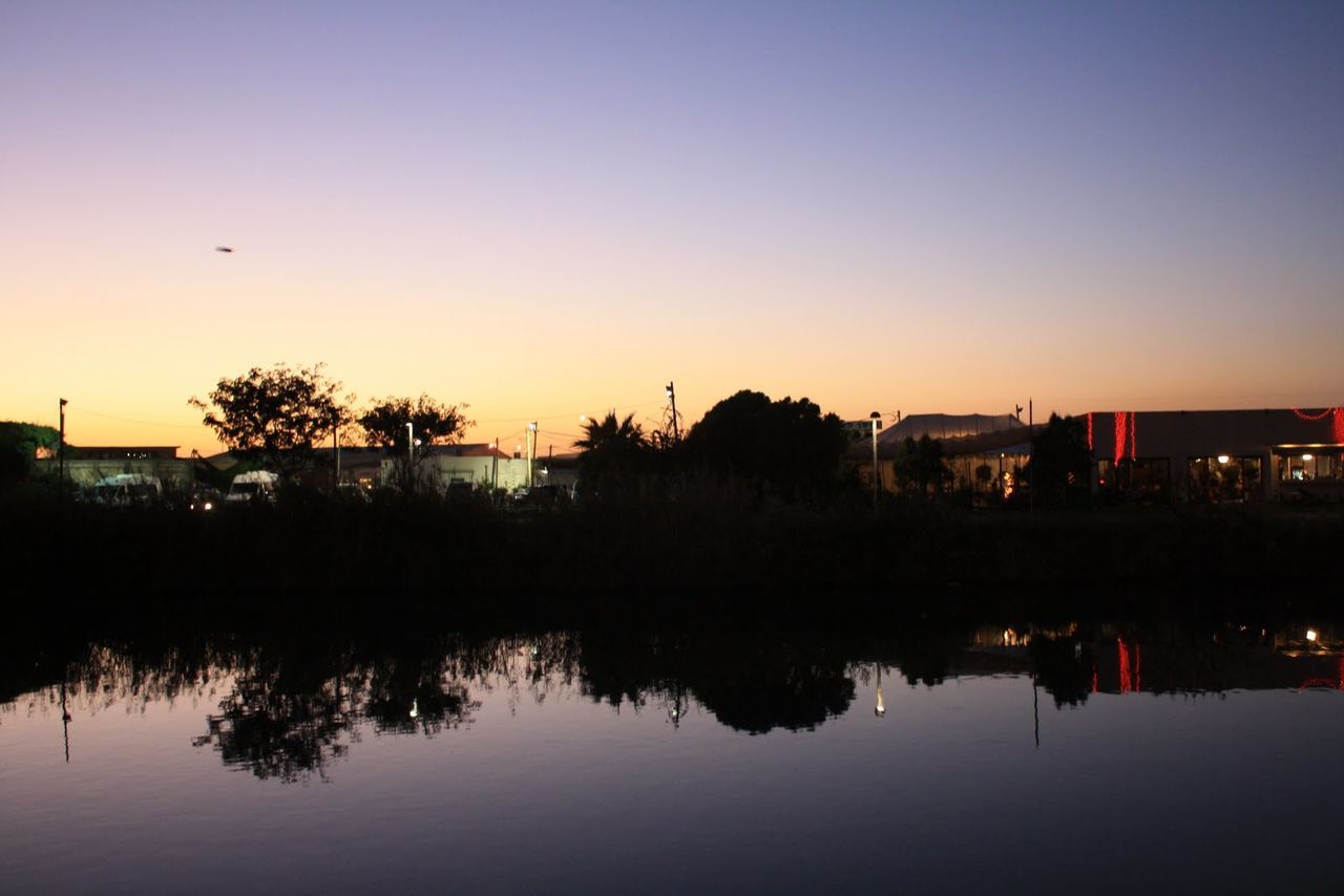 water, reflection, waterfront, sunset, architecture, built structure, tree, illuminated, tranquility, scenics, tranquil scene, city, sky, beauty in nature, nature, calm, outdoors, standing water, no people, blue, idyllic, growth