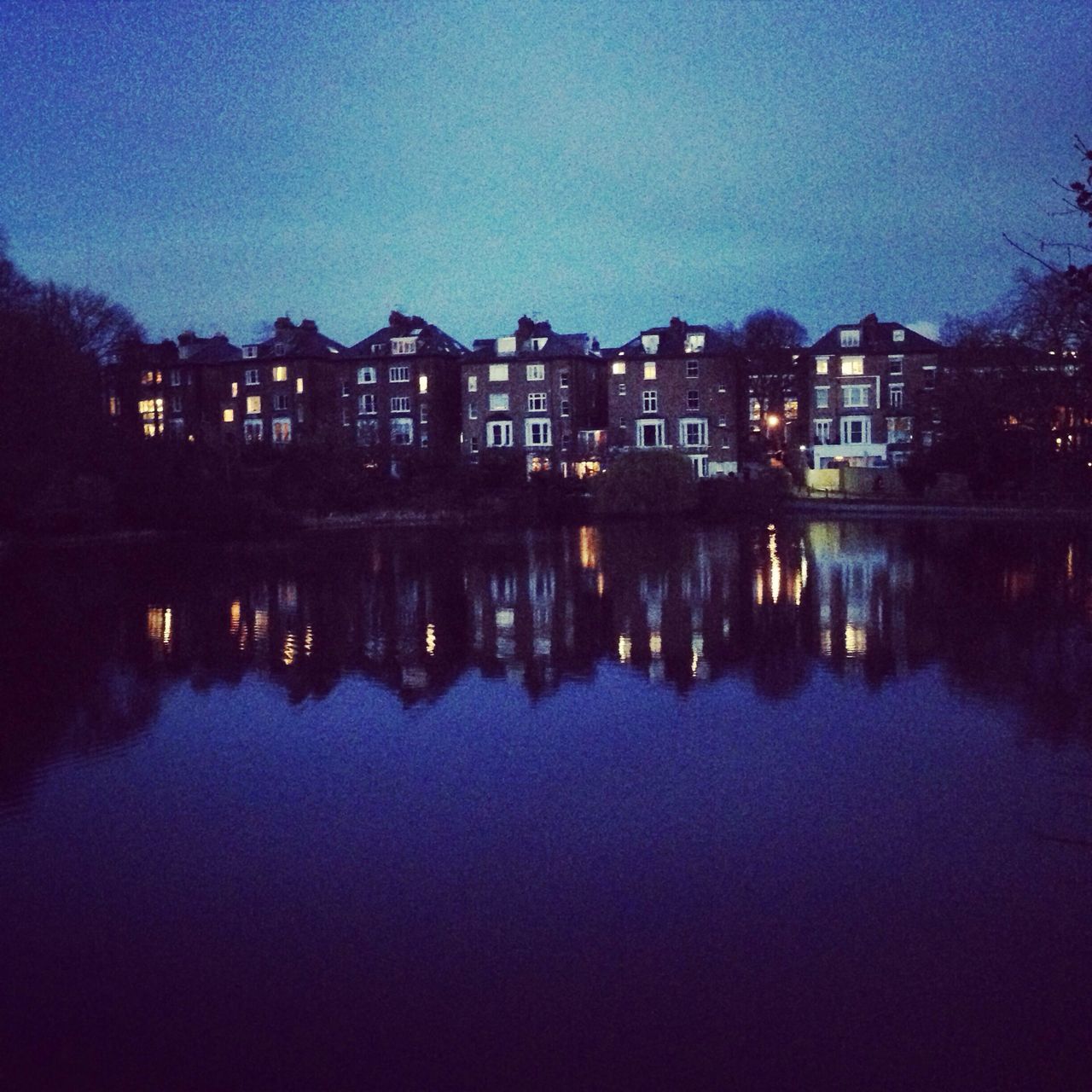 architecture, building exterior, built structure, water, reflection, waterfront, illuminated, river, city, standing water, lake, blue, sky, night, clear sky, residential building, tree, dusk, residential structure, building