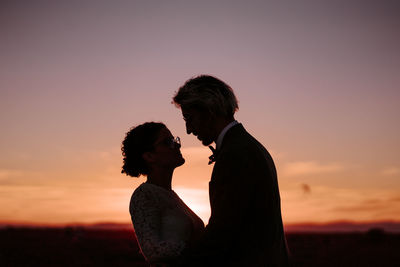 Side view of couple standing against orange sky