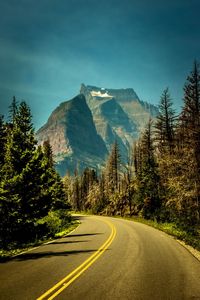 Road amidst trees and mountains against sky