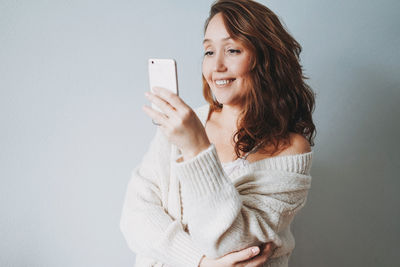 Attractive friendly smiling brunette woman middle age in cozy knitted cardigan using mobile isolated 