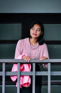 Portrait of smiling woman standing against railing