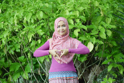 Portrait of woman in hijab gesturing against plants