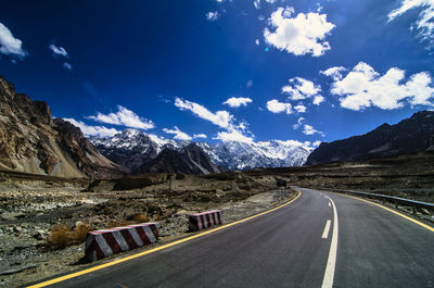 Country road leading towards mountains against sky