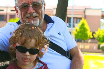 Portrait of grandfather mature man wearing sunglasses sitting on bench with nephew