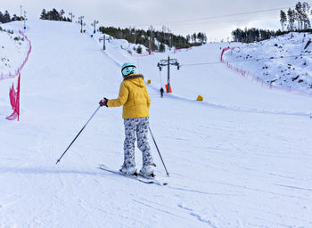 Rear view of young woman in yellow jacket and ski helmet skiing on mountain slope, winter sports